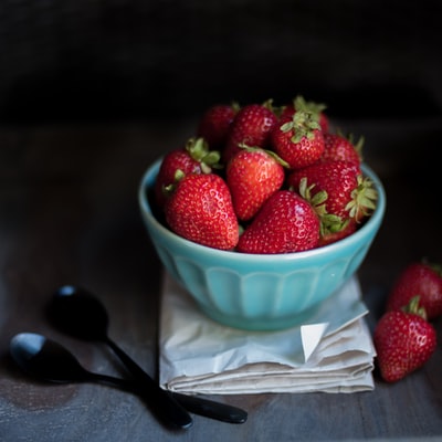 草莓水果放在两个黑色勺子旁边的蓝色陶瓷碗里